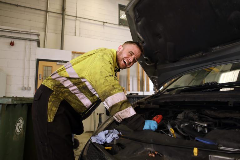 Image of apprentice wearing a hi-vis jacket repairing an engine
