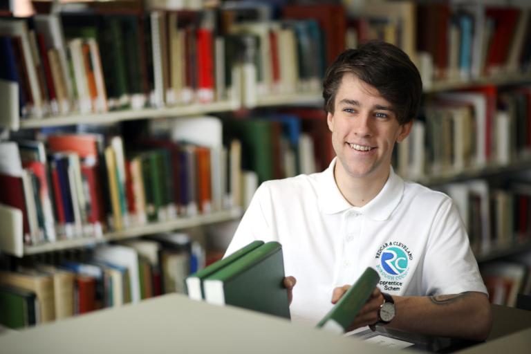 Image of apprentice wearing a white tshirt putting books on a shelf