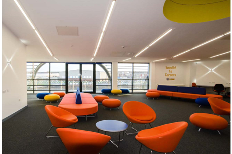 Image of the chill out area in the centre with two long circular couches, modern chairs and neon lights on the ceiling.