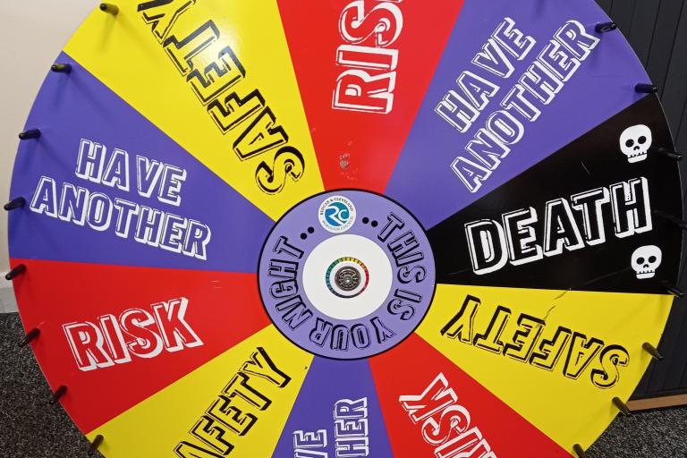 The drug wheel used in one of the activities of the Youth Work Plus. It is a spinning wheel which has the words risk, safety, have another and death, placed on different tiles in an alternating manner