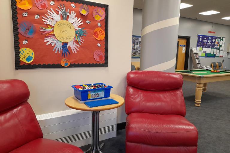 Image of a crafted poster created by the children attending the project with their handprints and a central design created with the outline of their hands. The piece is placed in a play room. 