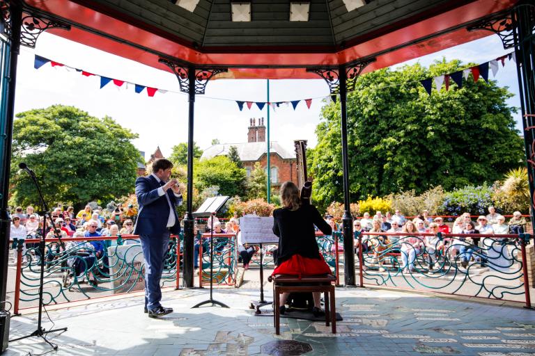 Harpist Sarah Paterson and Flutist James Cairns at the Saltburn Bandstand giving a performance in front of an audience - back view.