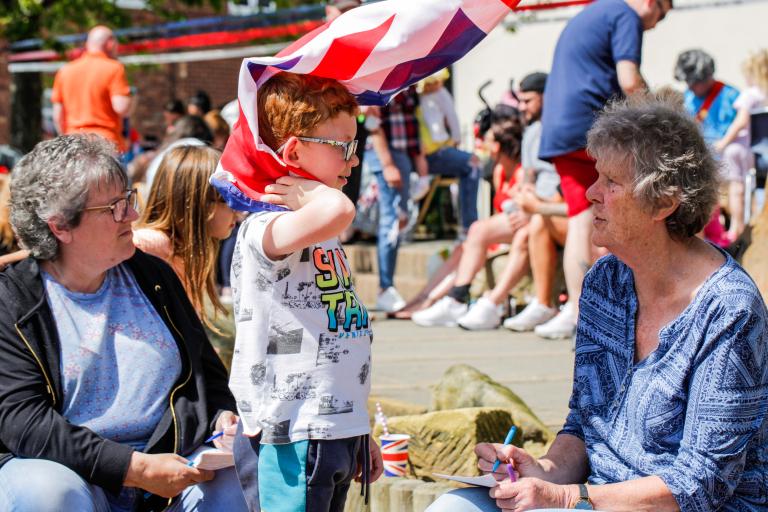 Image of a boy speaking with his grandmother and holding the Great Britain's flag at a street party in Loftus.