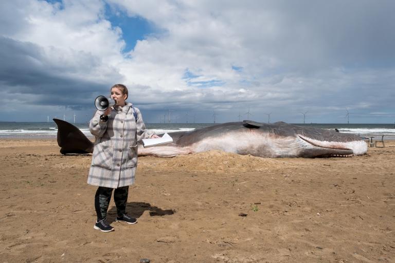 Image of an actress pretending to be protestor standing in front of the whale with a megaphone and talking about climate change 