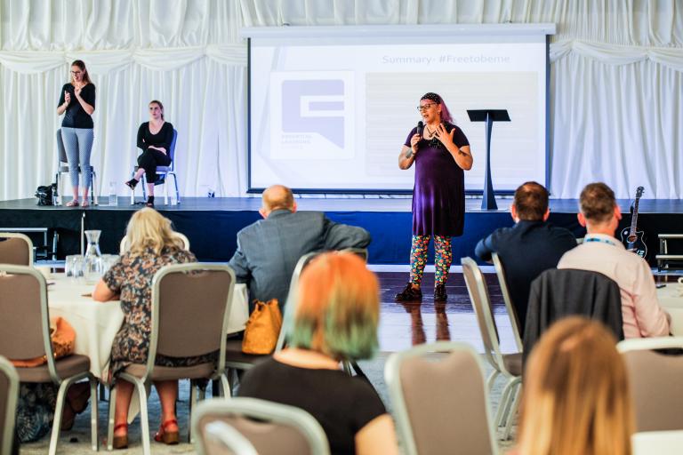 Ellie Lowther speaking at the Equality and Diversity conference. Behind her there are two sign-language translators.
