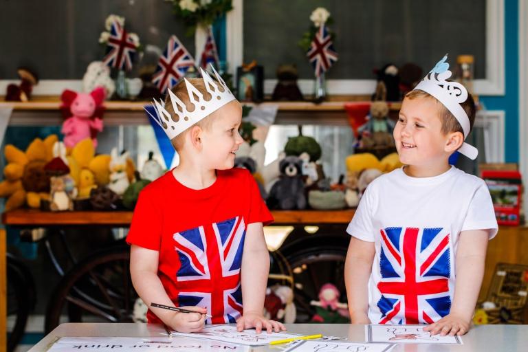 Twins wearing matching crowns and t-shirts with the UK flag smiling at each other at the Tea Party at Kirkleatham Museum