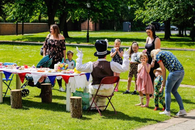 Image of the Mad Hatter at Tea Party Kirkleatham Museum, entertaining the children and parents at the long table filled with food and sweets..