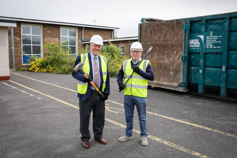 Image of Councillor Steve Kay and Councillor Chris Gallacher, dressed in safety equipment and holding construction tools, in front of the Eston swimming pool