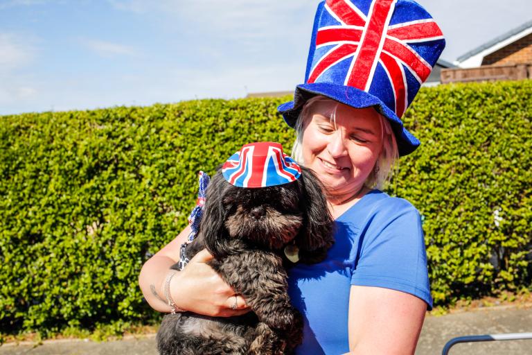 A woman with her dog at a street party. They are both wearing hats with the Great Britain's flag pattern.