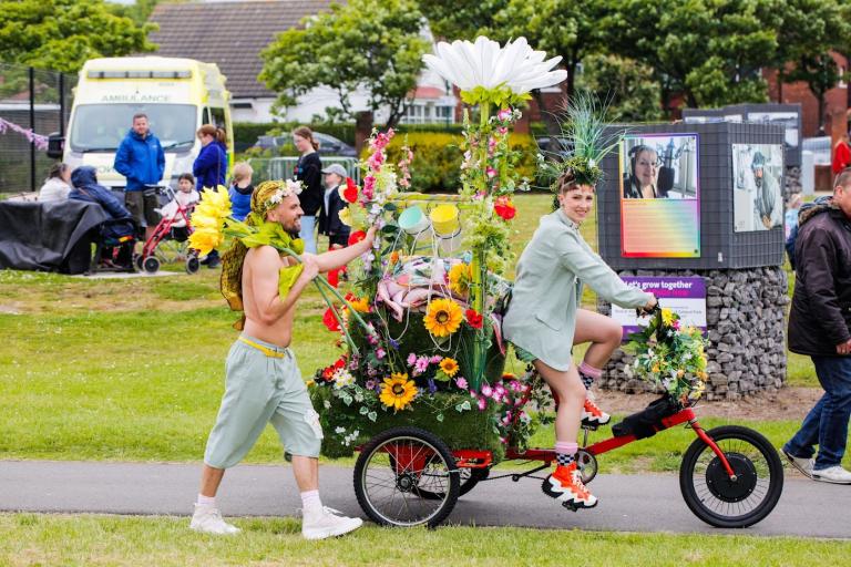 Two artists and performers with a bicycle decorated with flowers in Zetland Park.