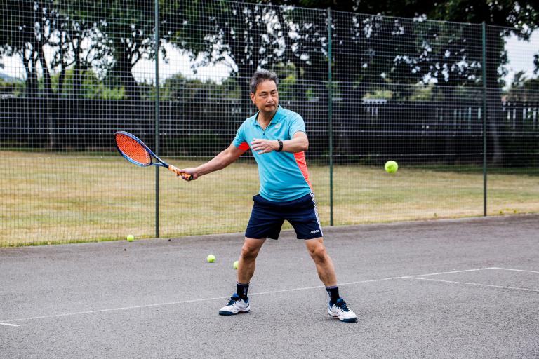 A man dressed in a blue t-shirt, playing tennis in the tennis court from Borough Park.