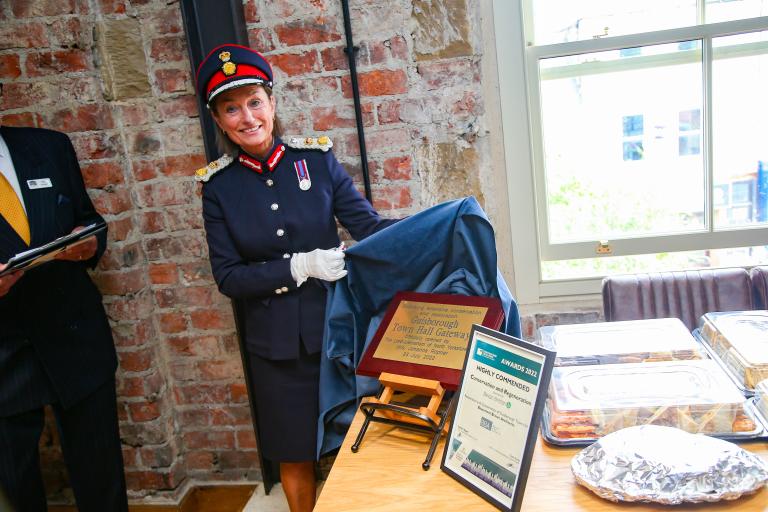 Image of Lord Lieutenant, Mrs Johanna Ropner, unveiling the gold plaque to commemorate the opening of Guisborough Town Hall which reads 'Guisborough Town Hall was officially opened by the Lord Lieutenant on 23 July 2022.