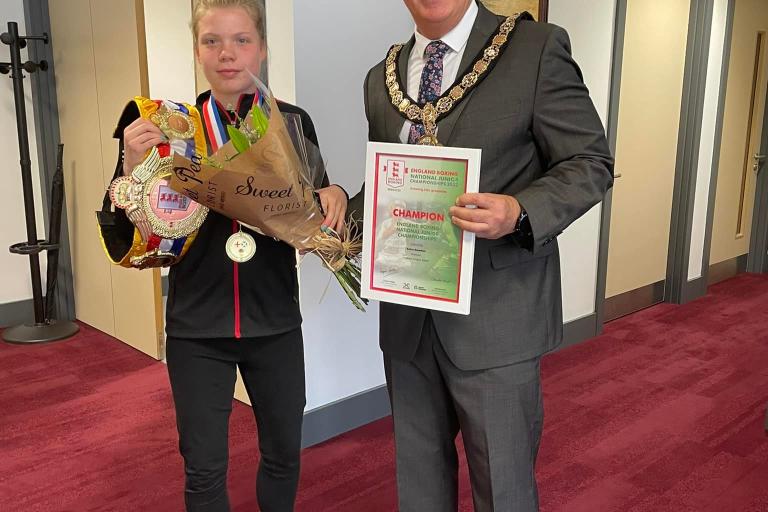 Image of Keira and Stuart. Keira is holding her boxing title and a bunch of flowers. Stuart is holding a certificate that says 'champion'.