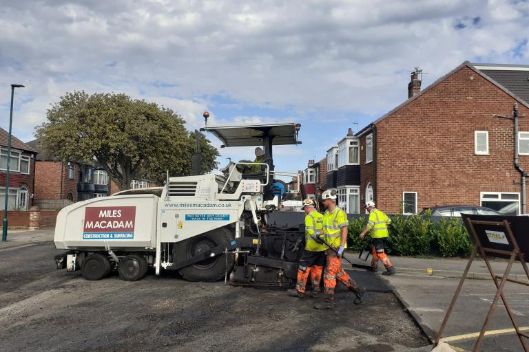 Image of workers operating an asphalt paver to resurface a road.