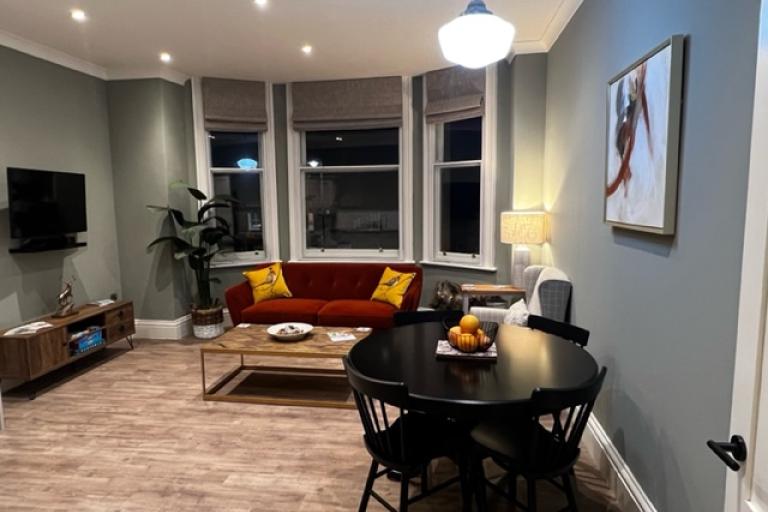 Image of the living room inside the newly refurbished Barclays Bank in Loftus. Inside the room there is a round table with four chairs, a red couch behind a coffee table, a TV and a TV stand.