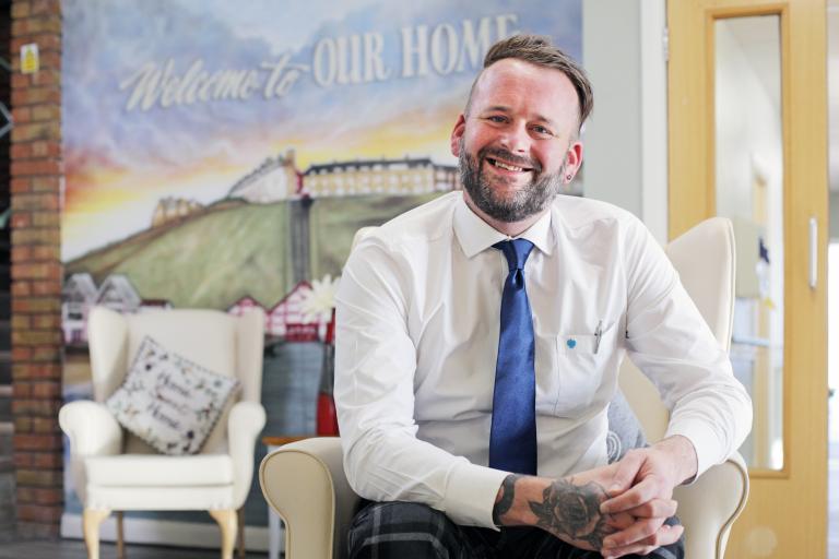 Image of a man dressed in a white shirt with a blue tie smiling at the camera.