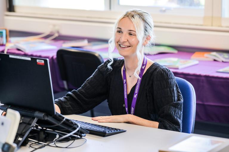 Image of a young woman sat at her desk and working on computer.