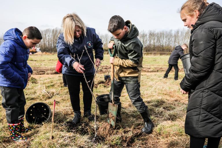 Image of school children planting a tree in the new community orchard with help from teachers.