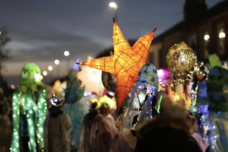 Image depicting last year's parade at the Christmas Lights Switch On with children carrying paper lanterns of different shapes such as stars.  