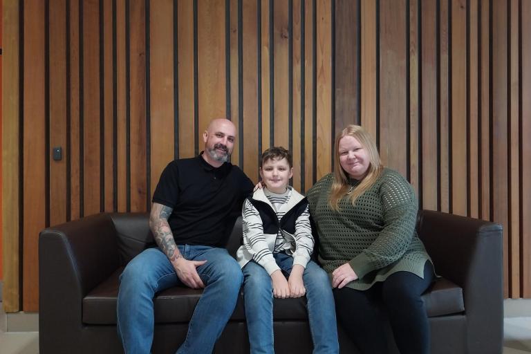 A man and a woman sitting on a couch with their boy in the middle.