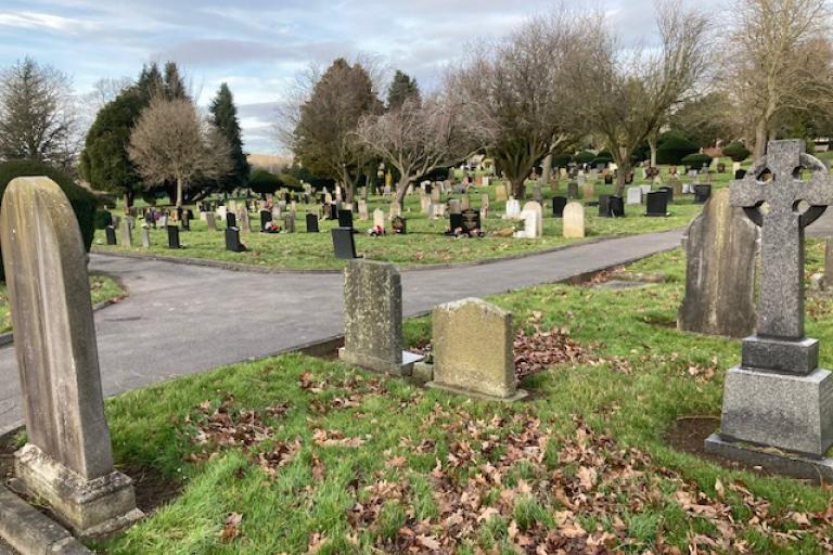Image of a cemetery. There are headstones in the foreground and background.