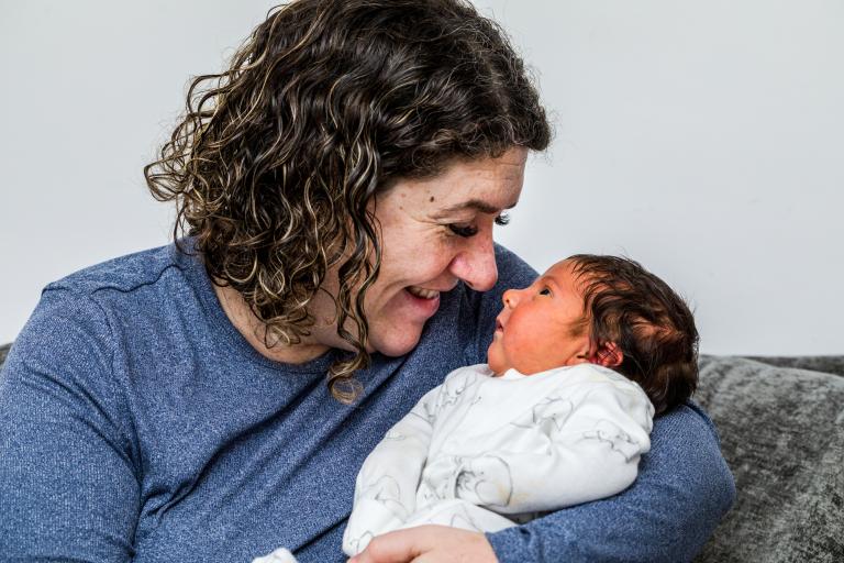 A woman holding her new born baby. The two of them are looking at each other and the mother is smiling.
