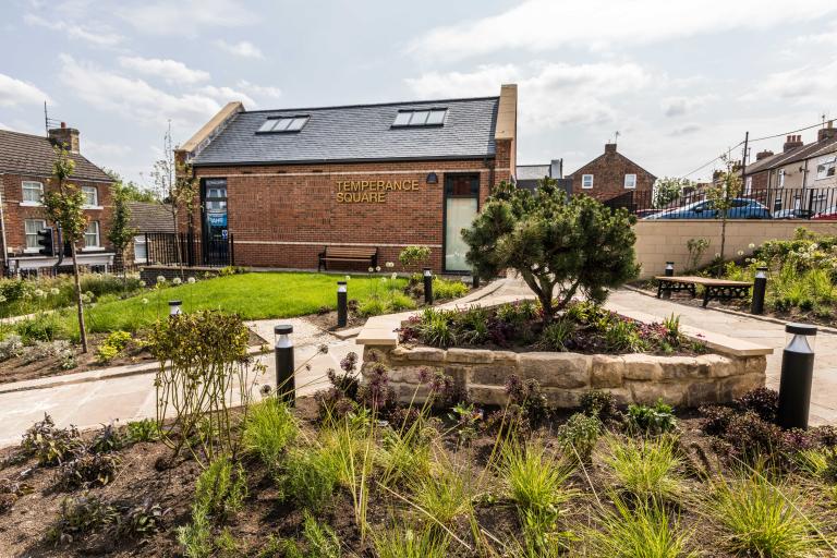 Image shows the temperance square building in loftus. In the foreground is a small grassed area. 