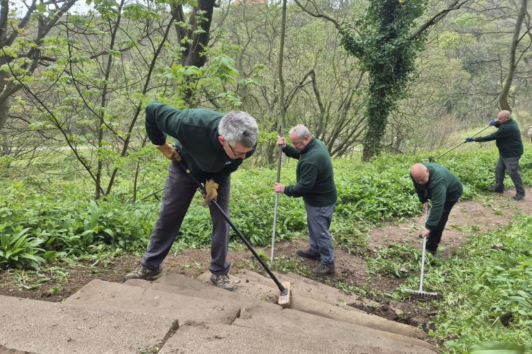 Four men brushing up a countryside path surrounded by trees and vegetation