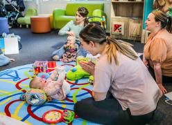 Babies sitting on a mat and playing with their mothers.