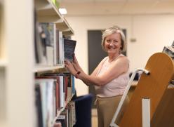 Image of a woman wearing a white shirt putting books on a shelf.