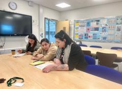 Image of three woman sat on blue seats looking over notes on a table.