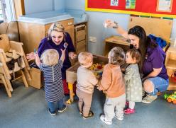 image of two women in purple shirts entertaining 4 toddlers.
