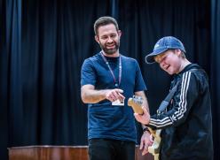 Image of two men. One is playing a guitar and the other is showing him how to play the guitar. 