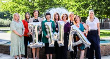Image of 9 women in front of a fountain holding balloons that are the letters I,W and A.