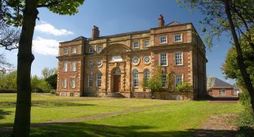 Image of Kirkleatham Museum on a summer day. The building is made up of light yellow and brown bricks.