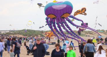 Image from the 2024 kite festival. The image shows a crowd of people on a beach with a purple octopus kite in the background.