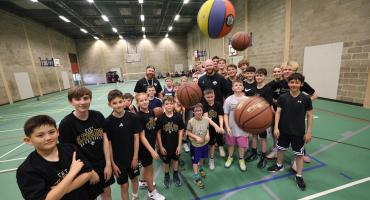 Image of members of the East Cleveland Basketball Club. There are balls bouncing toward the foreground with junior and adult members wearing black in the background.