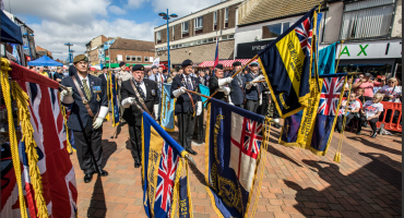 Image of a military parade. The uniformed men are lowering various flags in the foreground.