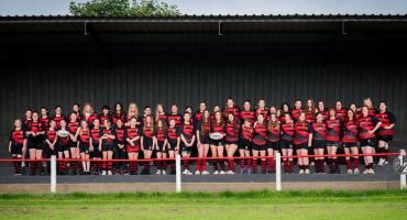 Image of Redcar Rugby Club's womens team. The women are in three rows wearing their kit, which is red and black