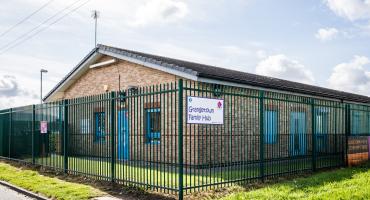Picture of a ne floor building surrounded by green grass and a fence with a sign reading "Grangetown Family Hub""