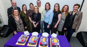 Image of staff from children's service stood in front of a cake that spells out the word 'good'