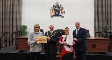 Two man and two women standing in the Council's chambers with the Redcar and Cleveland emblem behind them. They are holding two certificates attesting the council is an endometriosis friendly employer