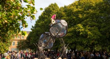 Image shows a man dressed in red climbing a tower with a crowd below