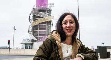 In the foreground there is a woman wearing a coat and smiling and in the background you can see the Redcar Beacon