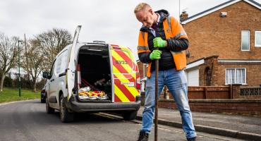 Image of a man wearing a hi-vis jacket filling a pothole. His van is in the background.