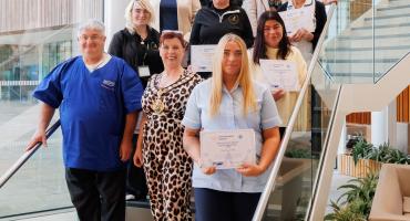 A picture of several men and women standing on the stairs inside a building, some of them holding certificates