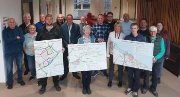 A group of people gathered in a room and smiling. The three people at the front are each holding a board showing a different area of the borough.