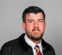 Image of Cllr David Taylor. Cllr Taylor is situated in the centre of the frame and is wearing a blue jacket over a white shirt and multicoloured tie. 