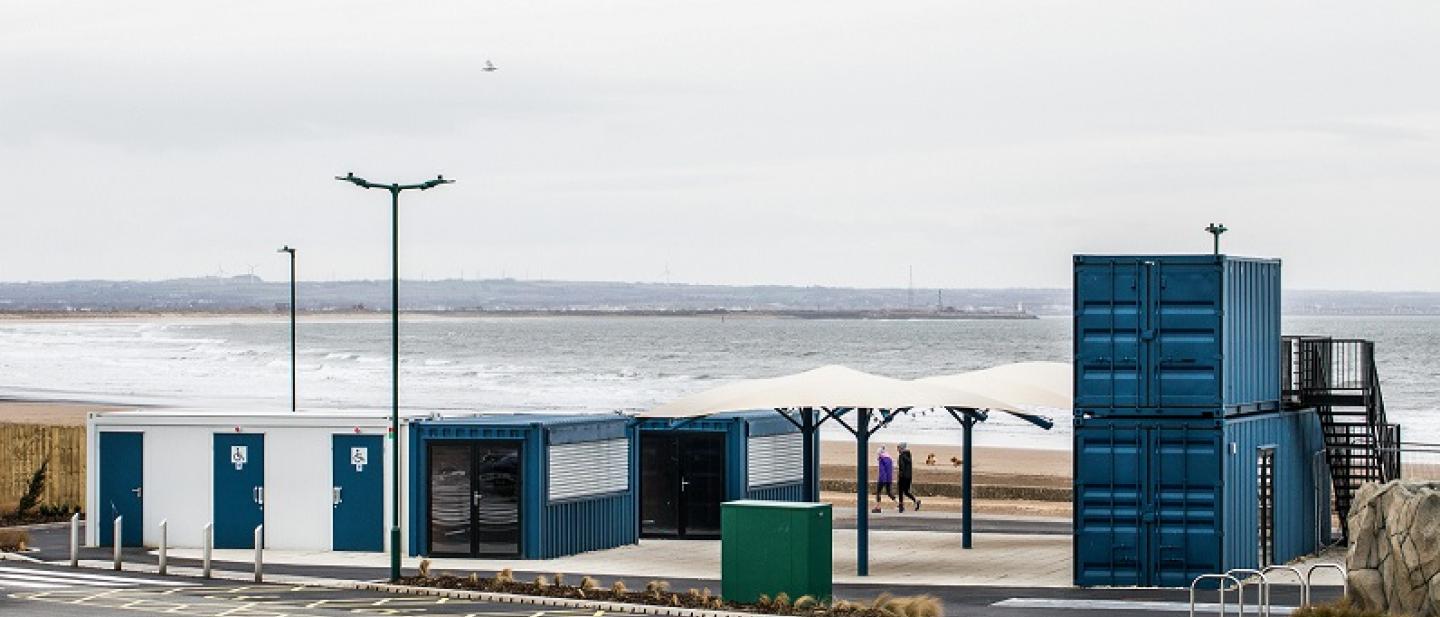 Image of blue containers on a seafront. You can see waves in the background.