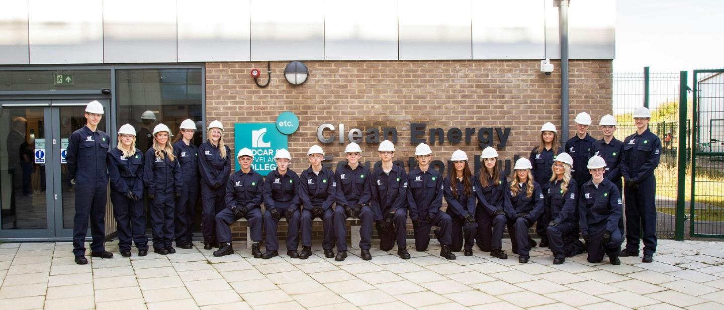 Image of students standing outside of Redcar college. They are wearing blue overalls with white helmets.